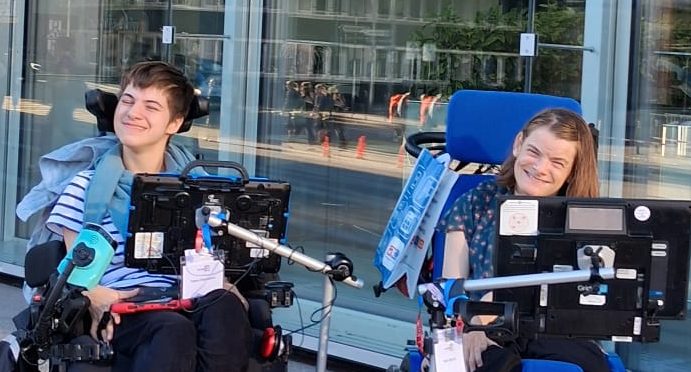 Tabea Engelmeier und Nele Diercks nebeneinander vor dem Tagungshaus, beide an ihren Sprachcomputern